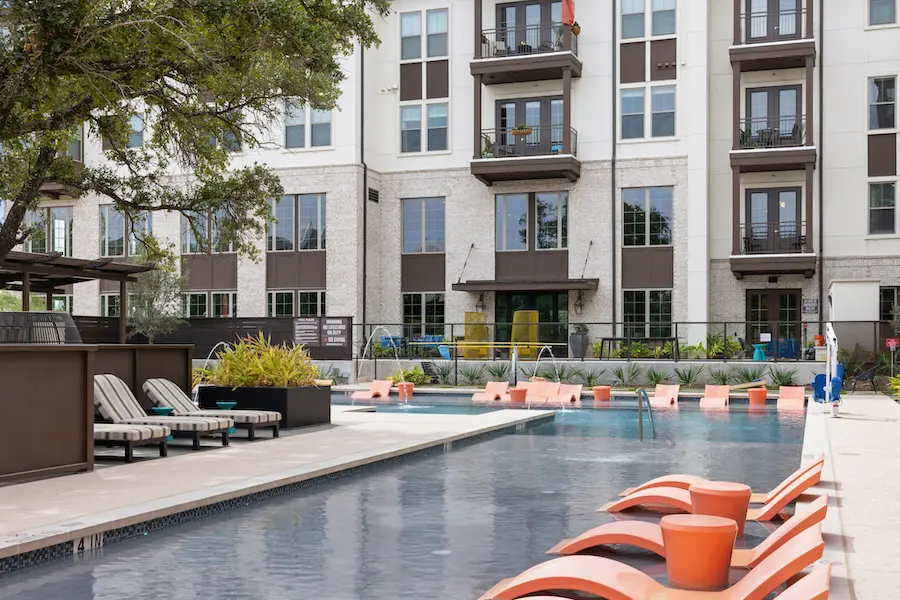 A pool with orange chairs and an apartment building in the background.